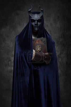 Foto de Retrato de oración de culto esotérico vestido con túnica oscura y máscara con cuernos. - Imagen libre de derechos