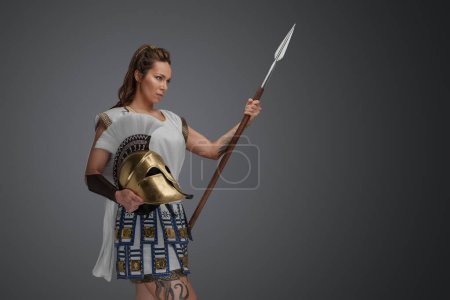 Foto de Shot of determined greek soldier woman dressed in armor and holding spear with helmet. - Imagen libre de derechos