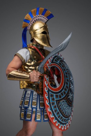 Foto de Estudio de tiro de guerrero griego antiguo con espada y escudo contra fondo gris. - Imagen libre de derechos