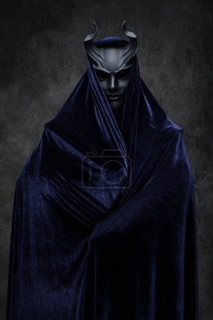 Téléchargez les photos : Plan studio d'un disciple du culte sombre vêtu d'une robe sombre et d'un masque à cornes. - en image libre de droit