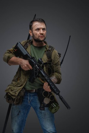 Foto de Studio shot of isolated on grey background military man with rifle survived after armageddon. - Imagen libre de derechos