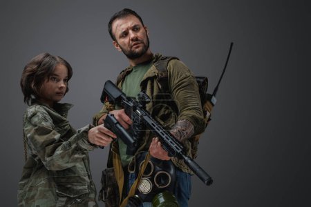Téléchargez les photos : Plan studio de l'homme militaire post-apocalyptique protégeant la jeune fille sur fond gris. - en image libre de droit