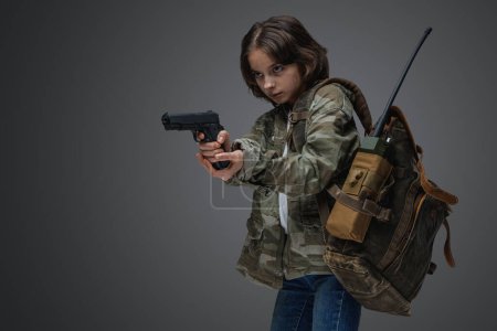 Foto de Retrato de niña sobreviviente con ropa de camuflaje sosteniendo pistola en el ajuste del apocalipsis posterior. - Imagen libre de derechos
