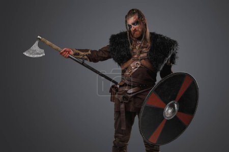 Photo for Studio shot of redhead nordic warrior from past holding shield and axe. - Royalty Free Image