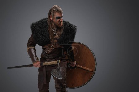 Téléchargez les photos : Portrait de barbare violent du nord avec peau de cerf et armure sur fond gris. - en image libre de droit