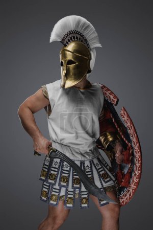 Téléchargez les photos : Prise de vue du soldat grec antique avec casque doré tenant bouclier arrondi et gladius. - en image libre de droit