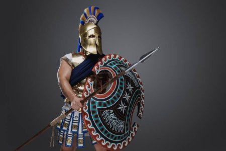Téléchargez les photos : Prise de vue d'un soldat grec vêtu d'un casque et d'une armure tenant une longue lance et un bouclier arrondi. - en image libre de droit