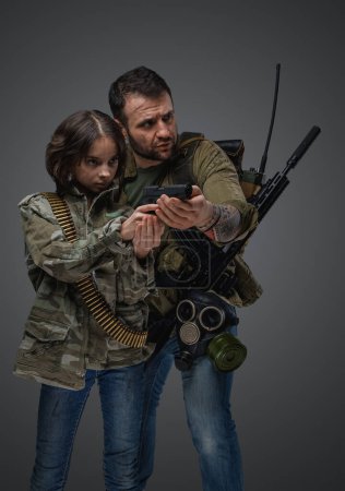 Foto de Portrait of post apocalyptic man teaching little girl to shoot in setting of post apocalypse. - Imagen libre de derechos