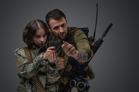 Téléchargez les photos : Portrait of post apocalyptic man teaching little girl to shoot in setting of post apocalypse. - en image libre de droit