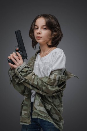 Téléchargez les photos : Prise de vue de jeune fille courageuse post apocalyptique vêtue d'une veste de camouflage tenant une arme de poing. - en image libre de droit