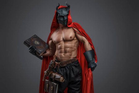 Studio shot of handsome fanatic of dark cult dressed in horned mask and red cloak.