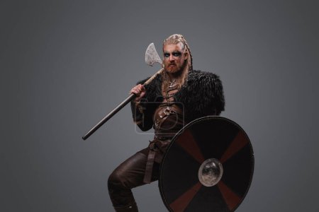 Foto de Estudio de temible bárbaro nórdico con hacha con escudo vestido de piel negra. - Imagen libre de derechos
