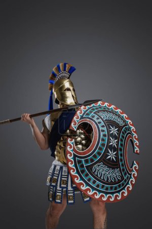 Foto de Tiro de soldado griego vestido con casco y armadura sosteniendo lanza larga y escudo redondeado. - Imagen libre de derechos