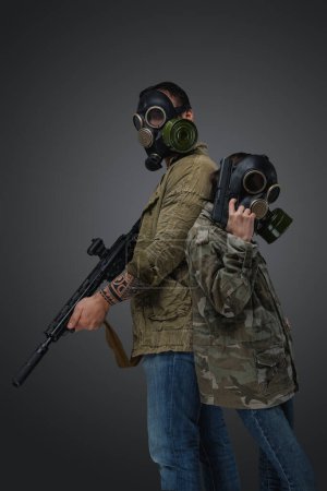 Foto de Shot of adult man and young girl in post apocalyptic style with gas masks and guns. - Imagen libre de derechos