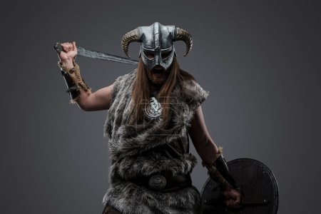 Photo for Shot of furious vandal from north dressed in helmet and fur holding sword and shield. - Royalty Free Image