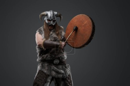 Photo for Portrait of barbaric warrior from north with drum dressed in fur and helmet. - Royalty Free Image