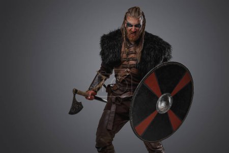 Téléchargez les photos : Prise de vue de guerrier nordique furieux vêtu d'armure en cuir et de fourrure sur fond gris. - en image libre de droit