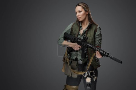 Foto de Tiro de estudio de mujer asesina profesional con rifle en el ajuste del apocalipsis posterior. - Imagen libre de derechos