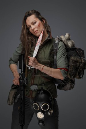 Photo for Portrait of female killer with gun and knife carrying backpack against grey background. - Royalty Free Image