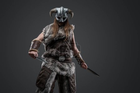 Téléchargez les photos : Prise de vue de Viking à poils longs du passé avec fourrure et casque tenant deux poignards. - en image libre de droit