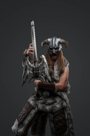 Portrait of viking in ecstasy dressed in fur and helmet playing electric guitar.