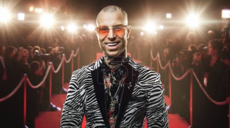 Téléchargez les photos : Prise de vue d'un riche tatoué vêtu d'un costume tendance et de lunettes posant sur un tapis rouge. - en image libre de droit