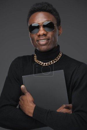 Photo for Studio shot of smiling black man with book dressed in sunglasses and golden chain. - Royalty Free Image