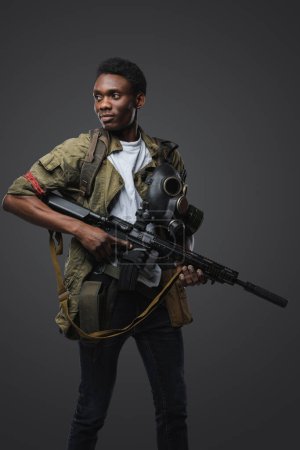 Foto de Disparo de soldado negro en escenario post apocalíptico vestido con uniforme y rifle de mano. - Imagen libre de derechos