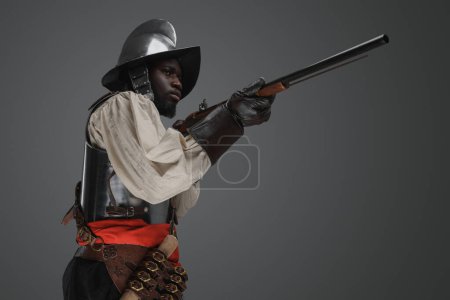 Photo for Shot of medieval soldier dressed in steel armor and helmet aiming flintlock musket. - Royalty Free Image