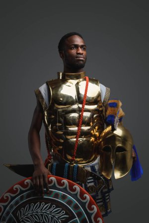 Foto de Disparo de soldado griego antiguo de etnia africana con escudo y armadura dorada. - Imagen libre de derechos