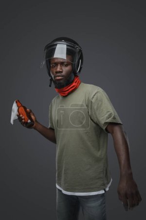 Photo for Portrait of aggressive black man dressed in casual attire and helmet holding molotov cocktail. - Royalty Free Image