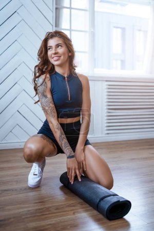 Photo for Domestic sport and leisire. Portrait of a seductive and joyful sportswoman preparing to workout on floor in modern room. - Royalty Free Image