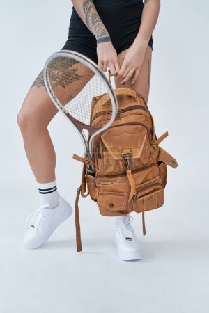 Photo for Healthy and sportive lifestyle. Sports gear. Bottom view of a female athlete carrying backpack with tennis racket in white background. - Royalty Free Image