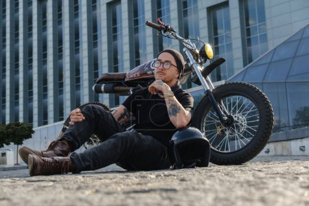 Foto de Tiro de conductor de motocicleta individual posando cerca de enorme edificio de la ciudad. - Imagen libre de derechos