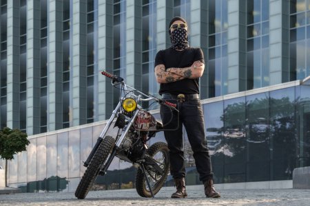 Photo for Portrait of tattooed urban biker with bandana and motorcycle posing with crossed arms. - Royalty Free Image