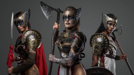 Studio shot of ancient amazons with cold steel dressed in armors against gray background.