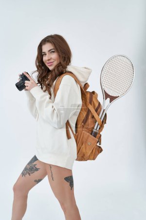 Foto de Retrato de una deportista alegre y bonita llevando bolsa y sosteniendo la cámara fotográfica en fondo blanco. - Imagen libre de derechos
