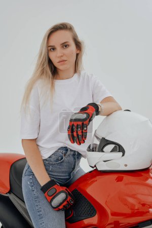 Téléchargez les photos : Prise de vue en studio d'une jeune conductrice de moto aux cheveux blonds isolés sur fond blanc. - en image libre de droit