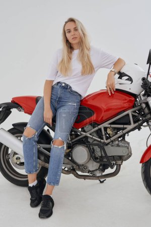 Photo for Shot of attractive blond woman weared in casual attire posing around bike against white background. - Royalty Free Image