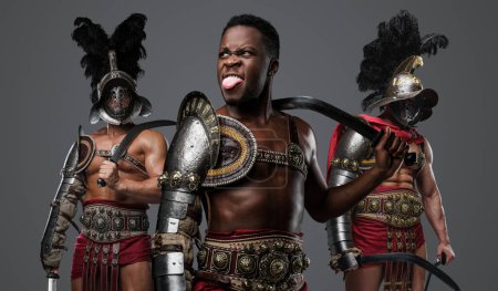 Téléchargez les photos : Portrait de gladiateur africain fou du passé avec épées jumelées et deux camarades. - en image libre de droit