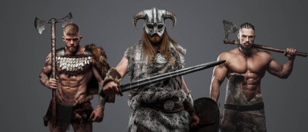 Foto de Estudio de vikingos musculosos vestidos de piel y armaduras armados con hachas y espadas. - Imagen libre de derechos