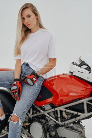 Photo for Studio shot of active woman with long blond hairs riding red motorbike against white background. - Royalty Free Image