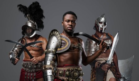 Téléchargez les photos : Portrait du beau gladiateur africain du passé avec des épées jumelées et deux camarades. - en image libre de droit