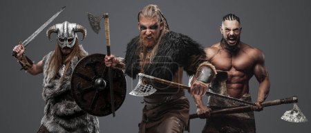 Foto de Tiro de grupo de tres vikingos vestidos de piel y armadura armados con hachas. - Imagen libre de derechos