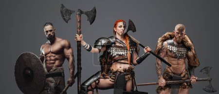 Photo for Shot of nordic amazon with red hairs with two fierce comrades with armour and axes. - Royalty Free Image