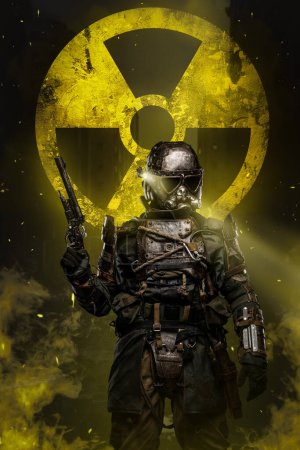 Téléchargez les photos : Le soldat post-apocalyptique se tient contre le signe jaune de protection nucléaire, tenant un fusil conceptuel et portant une armure anti-nucléaire unique conçue pour protéger contre les dangers d'une friche nucléaire - en image libre de droit