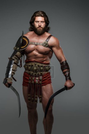 Photo for A fierce and imposing gladiator with long hair and a beard, donning light armor and standing tall with two swords. This warrior exudes strength and power against a neutral gray backdrop - Royalty Free Image