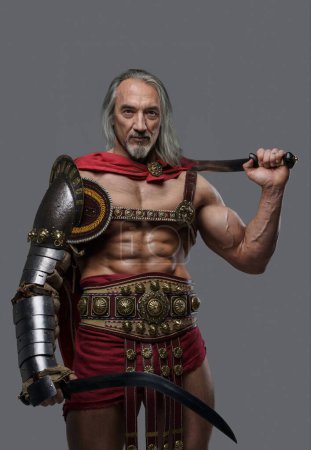 Photo for Distinguished elder gladiator exudes power and strength in elegant, lightweight armor, wielding two gladius swords with confidence against a grey background - Royalty Free Image