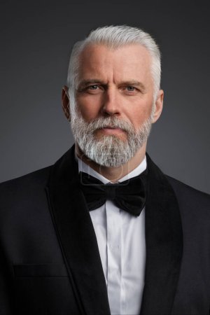 Photo for Distinguished older gentleman exudes confidence in this photo, dressed in a sharp black suit and bow tie. The grey background highlights his striking grey hair and determined pose - Royalty Free Image