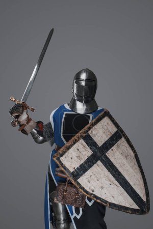 Foto de Azul vestido con sobretodo medieval caballero activamente balanceo espada en la batalla sobre fondo gris - Imagen libre de derechos